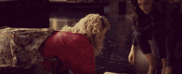 a woman in a red shirt is kneeling down next to another woman in a black shirt