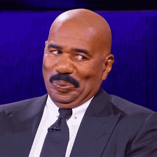 a bald man with a mustache wearing a suit and tie is making a funny face
