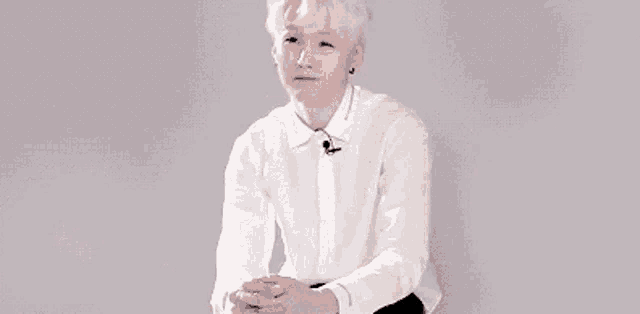a young man in a white shirt and black pants is sitting on a chair with his hands folded .
