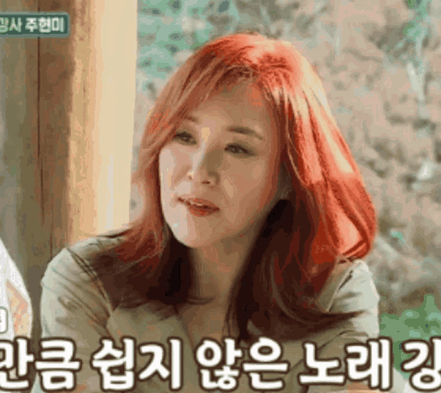 a woman with red hair is sitting in front of a sign with korean writing on it