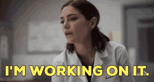 a woman in a white lab coat is saying i 'm working on it .