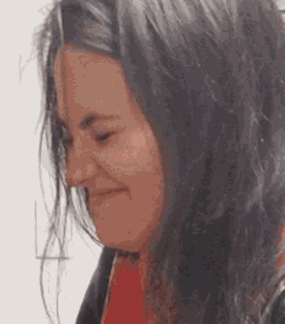 a woman with long black hair is smiling and wearing a red scarf around her neck .