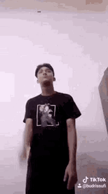 a man in a black shirt is standing in front of a wall .