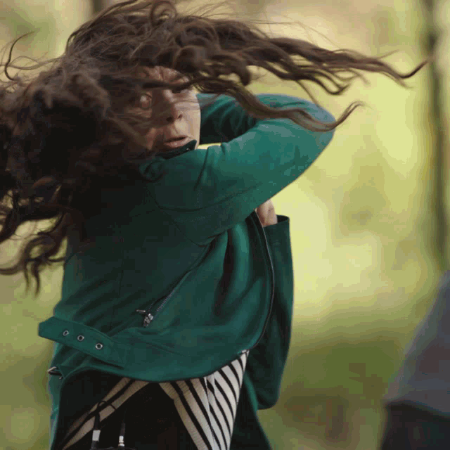 a woman in a green jacket with her hair blowing