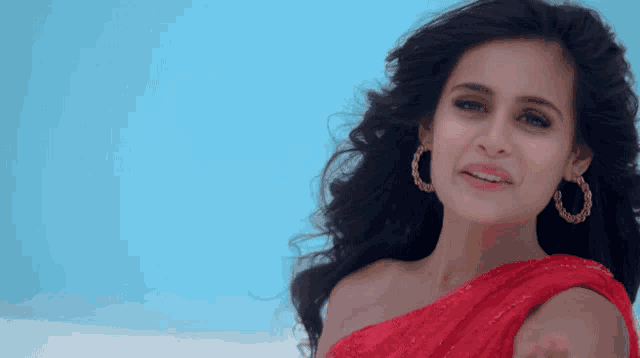a woman in a red dress and gold hoop earrings is smiling