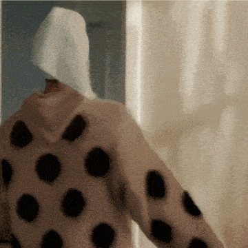 a person wearing a sweater with black polka dots and a white towel on their head