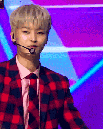 a young man wearing a plaid jacket and tie is speaking into a microphone