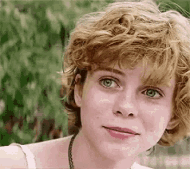 a close up of a woman 's face with curly hair and green eyes looking at the camera .