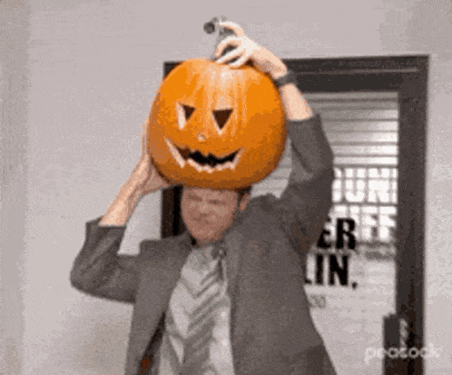 a man wearing a suit and tie is holding a pumpkin on his head .