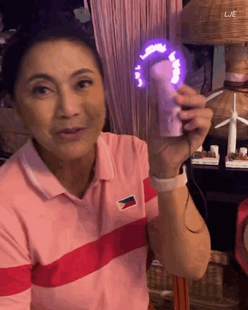 a woman in a pink and red polo shirt is holding a purple fan