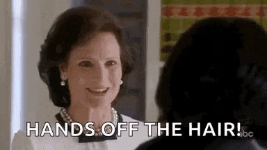 a woman is smiling while talking to another woman and says `` hands off the hair '' .