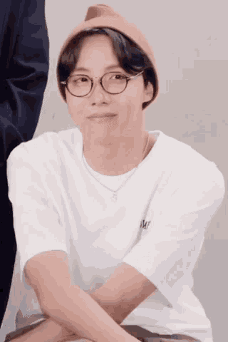 a young man wearing glasses and a beanie is sitting down with his arms crossed .