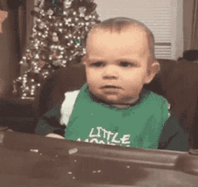 a baby is sitting in a chair with a christmas tree in the background and making a funny face .