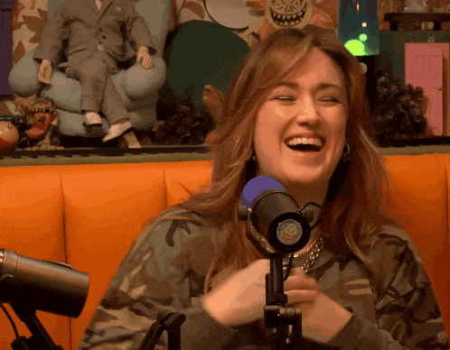 a woman in a camo sweatshirt is laughing in front of a microphone that has a smiley face on it