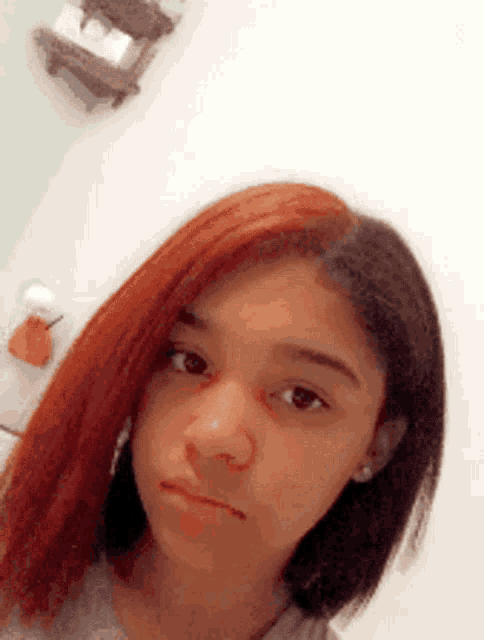 a girl with red hair is taking a selfie in front of a white wall .