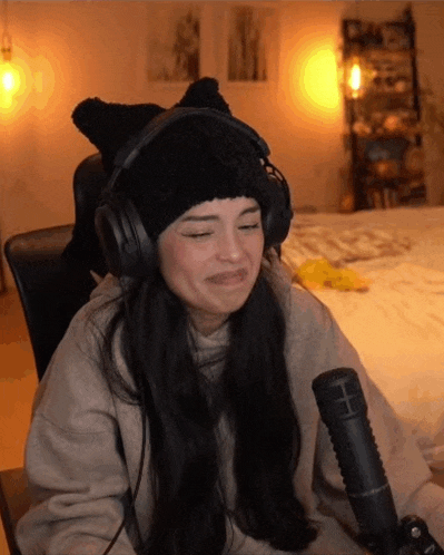 a woman wearing headphones and a cat hat is sitting in front of a microphone making a funny face .