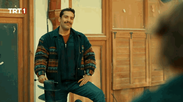 a man with a mustache is standing in front of a building that says trt1