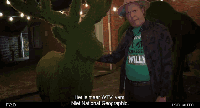 a man wearing a green shirt that says willy stands next to a statue of a deer