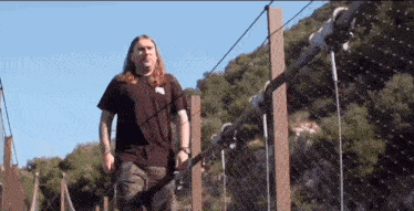 a man with long hair walking across a bridge