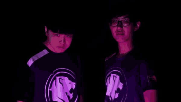 two young men wearing purple shirts with a lion on the front are standing next to each other in the dark .