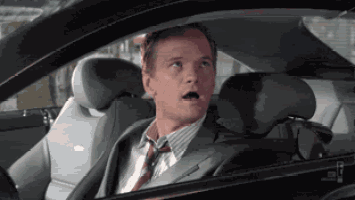 a man in a suit and tie is sitting in the driver 's seat of a car .