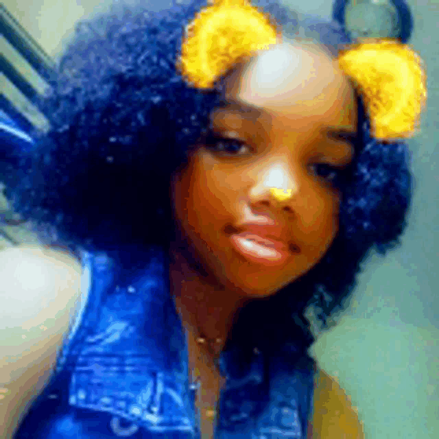 a young girl with curly hair is wearing a denim vest and a snapchat filter on her face .