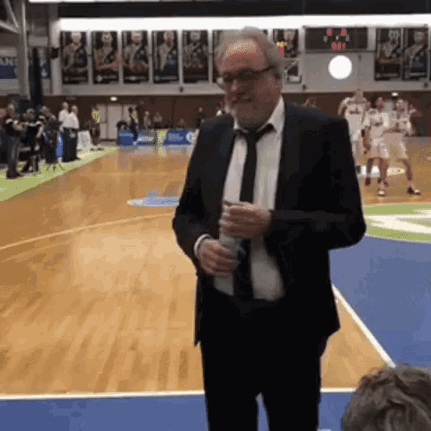 a man in a suit and tie stands on a basketball court holding a bottle of water