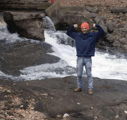 a man stands in front of a waterfall with his arms up