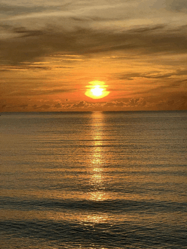 the sun is setting over the ocean with a few clouds in the sky