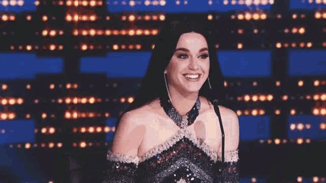 a woman in a dress is smiling while standing in front of a microphone on a stage .