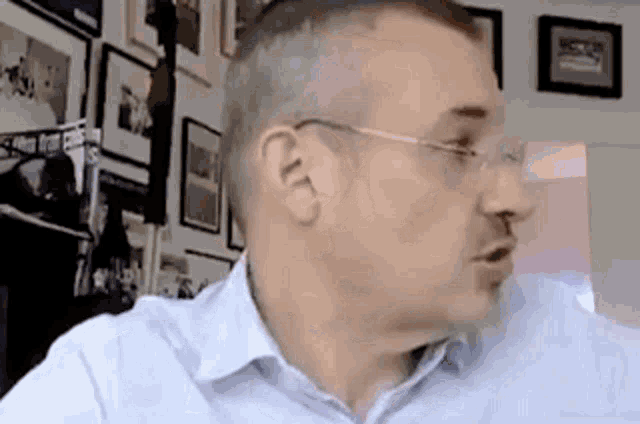 a man wearing glasses and a blue shirt is sitting in front of a wall of pictures .