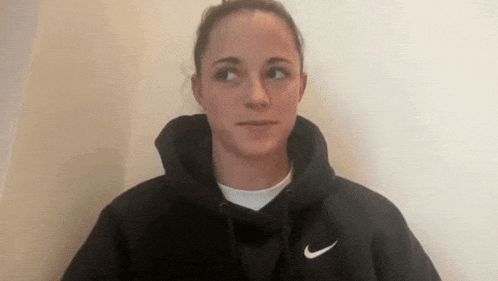 the woman is wearing a black nike hoodie and looking at the camera .