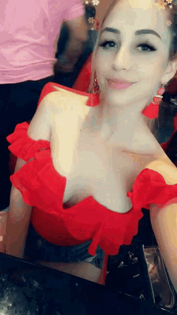 a woman in a red off the shoulder top is smiling for the camera