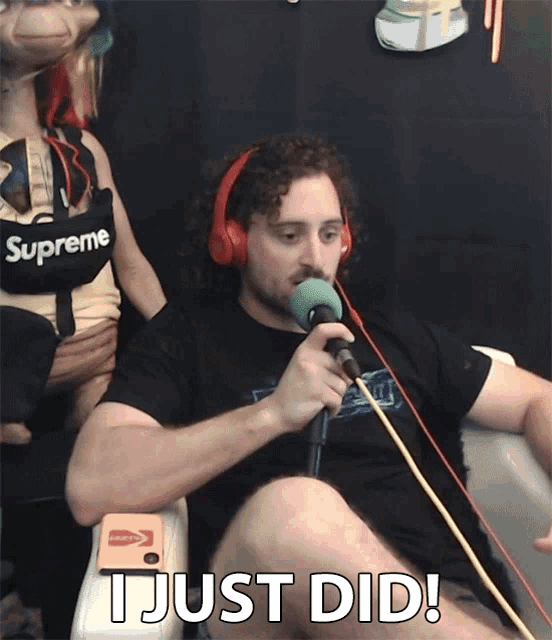 a man wearing headphones and a supreme shirt is sitting in front of a microphone
