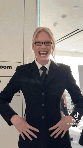 a woman wearing a suit and tie is laughing with her hands on her hips .