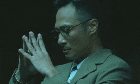 a man wearing glasses and a suit is praying with his hands folded
