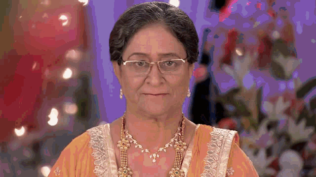 a woman wearing glasses and a necklace is smiling for the camera .