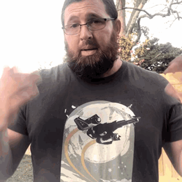 a man with a beard and glasses is wearing a t-shirt with a picture of two guns on it