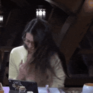 a woman wearing glasses is sitting at a table with a tablet on it