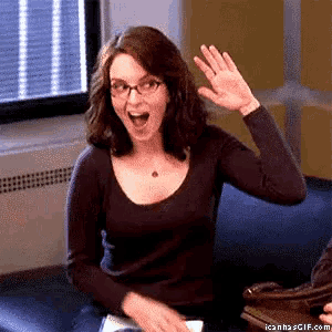a woman with glasses is sitting on a couch waving her hand