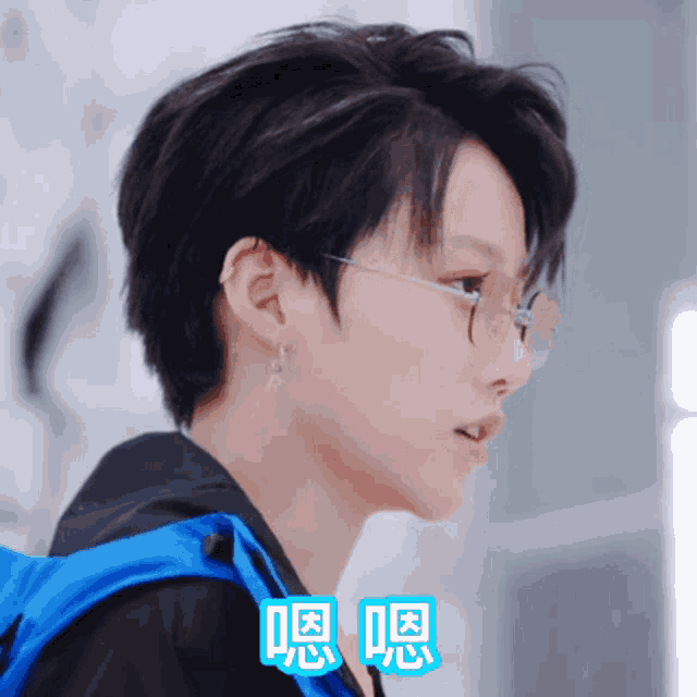 a close up of a person wearing glasses and a blue jacket with chinese writing on it