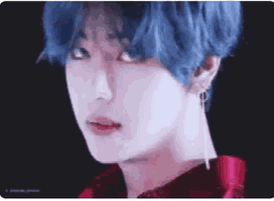 a close up of a person with blue hair wearing a red shirt and earrings .