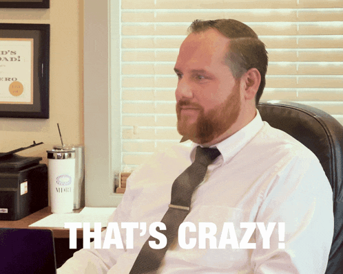 a man sitting at a desk with the words that 's crazy written on his shirt