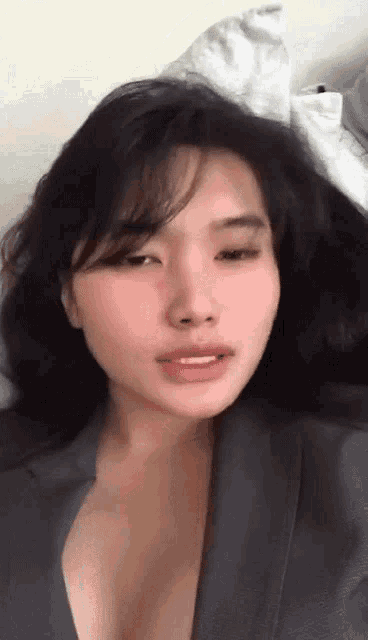 a close up of a woman 's face with her eyes closed and a gray jacket on .