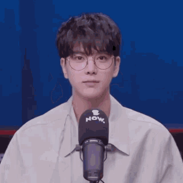 a young man with glasses is standing in front of a microphone .