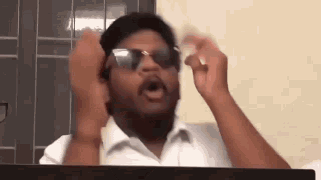 a man wearing sunglasses and a white shirt is sitting in front of a computer monitor .
