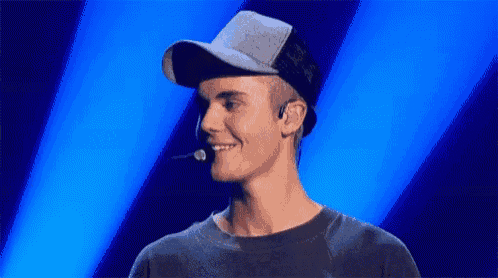 justin bieber is wearing a hat and headphones and smiling while standing in front of a microphone .
