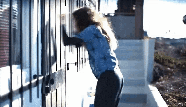 a woman in a blue shirt is standing in front of a door with a lock on it .