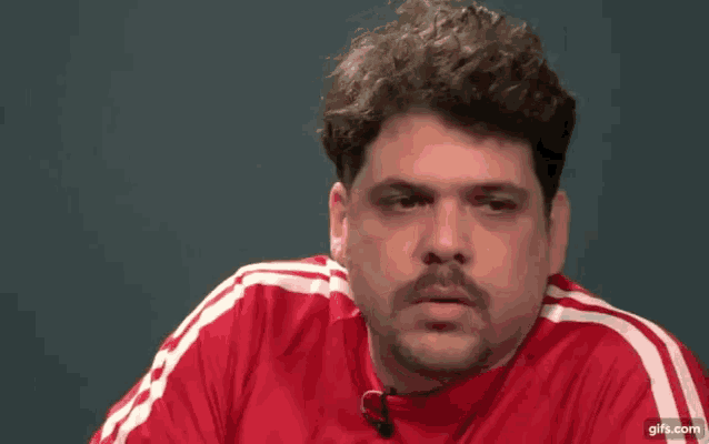 a man with a mustache is wearing a red adidas shirt .