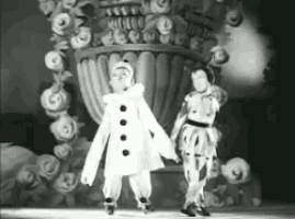 two clowns are dancing on a stage in front of a vase of roses .